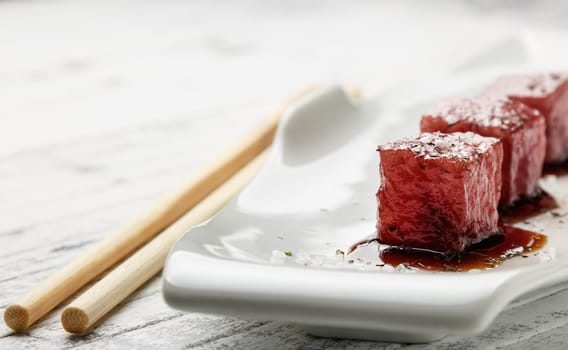 Tuna sashimi dipped in soy sauce,  thick salt and dill on old white wooden board with chopsticks. Raw fish in traditional Japanese style. Horizontal image.