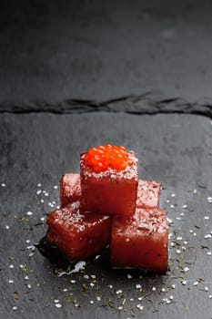 Tuna sashimi dipped in soy sauce with salmon roe, thick salt and dill on slate stone. Raw fish in traditional Japanese style. Vertical image.