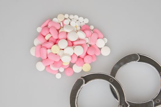 Silver handcuffs and stack of tablets place on white background.