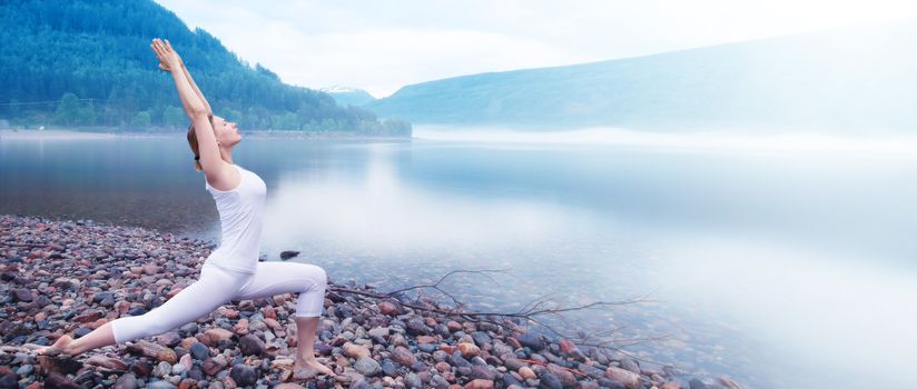 Young woman practice yoga on beach of foggy morning fjord in Norway