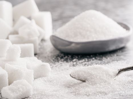 Sugar background. Sugar cubes, granulated sugar in spoon and plate. White sugar on gray galvanized iron background. Copy space.