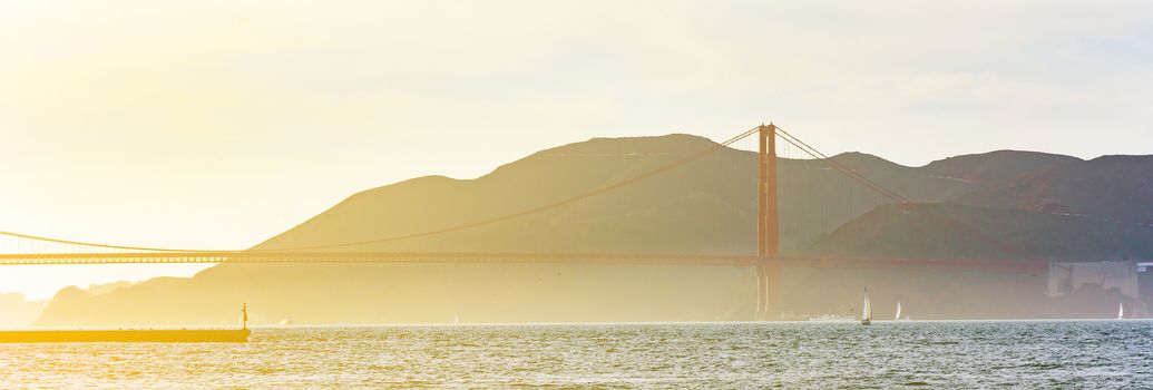 San Francisco bay area viewed from Pier 39 with foggy Golden Gate bridge in the distance in a bright sunset
