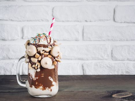 Close up view of freakshake in mason jar on brown table. Freaked milkshake with chocolate, biscuit cookies and sugar sprinkling. Copy space. Trendy food concept