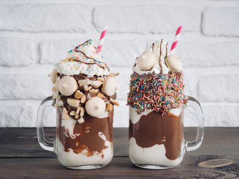 Close up view of two freakshake in mason jar on brown table. Freaked milkshake with chocolate, biscuit cookies and sugar sprinkling. Trendy food concept