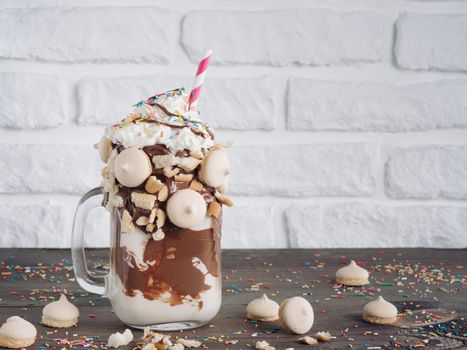 Close up view of freakshake in mason jar on brown table. Freaked milkshake with chocolate, biscuit cookies and sugar sprinkling. Copy space. Trendy food concept