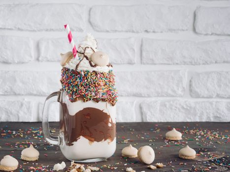 Close up view of freakshake in mason jar on brown table. Freaked milkshake with chocolate, biscuit cookies and sugar sprinkling. Copy space. Trendy food concept