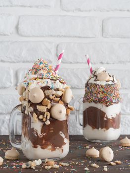 Close up view of two freakshake in mason jar on brown table. Freaked milkshake with chocolate, biscuit cookies and sugar sprinkling. Trendy food concept. Vertical.
