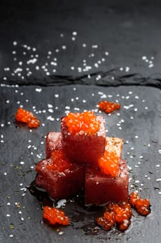 Tuna sashimi dipped in soy sauce with salmon roe, thick salt and dill on slate stone. Raw fish in traditional Japanese style. Vertical image.