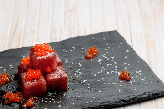 Tuna sashimi dipped in soy sauce with salmon roe, thick salt and dill on slate stone. Raw fish in traditional Japanese style. Horizontal image.