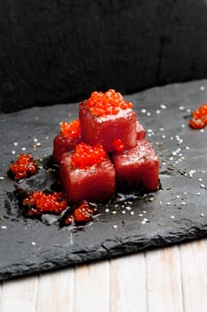 Tuna sashimi dipped in soy sauce with salmon roe, thick salt and dill on slate stone. Raw fish in traditional Japanese style. Vertical image.