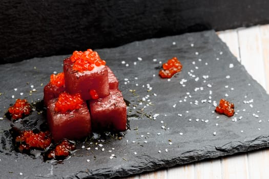 Tuna sashimi dipped in soy sauce with salmon roe, thick salt and dill on slate stone. Raw fish in traditional Japanese style. Horizontal image.