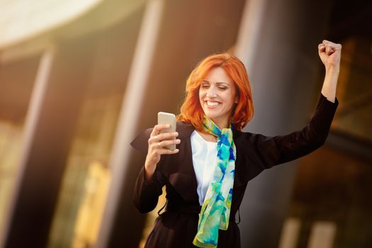 Smiling businesswoman using smartphone in office district after successful meeting.