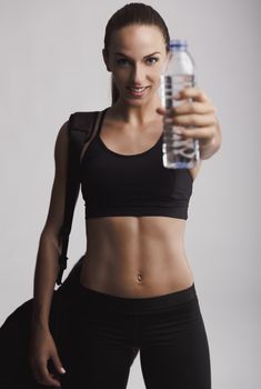Portrait of sporty young woman holding a water bottle, against a gray background