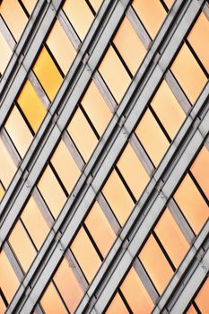 Orange colored glass windows of modern business office building at sunset in evening, diagonal perspective, low angle view, close up