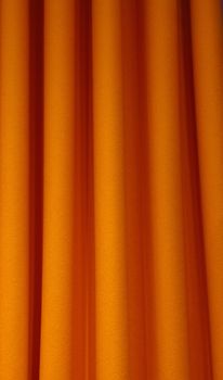 Heavy orange color pleated felt textile curtain background with portiere drape folds, side view close up