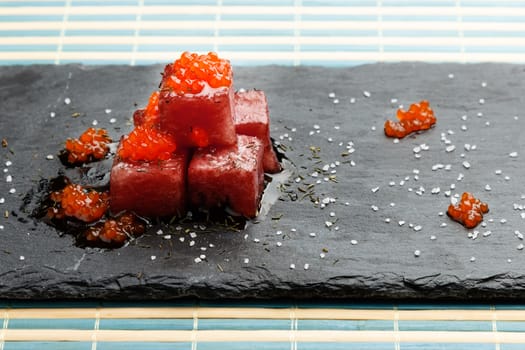 Tuna sashimi dipped in soy sauce with salmon roe, thick salt and dill on slate stone. Raw fish in traditional Japanese style. Horizontal image.