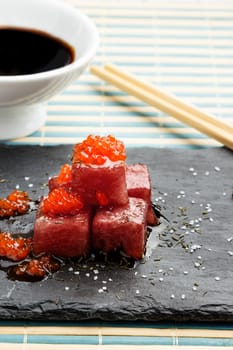 Tuna sashimi dipped in soy sauce with salmon roe, thick salt and dill on slate stone with chopsticks and bowl with soy. Raw fish in traditional Japanese style. Vertical image.