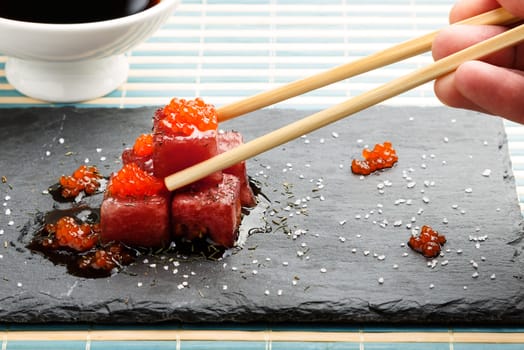 Tuna sashimi dipped in soy sauce with salmon roe, thick salt and dill on slate stone with chopsticks and bowl with soy. Raw fish in traditional Japanese style. Horizontal image.