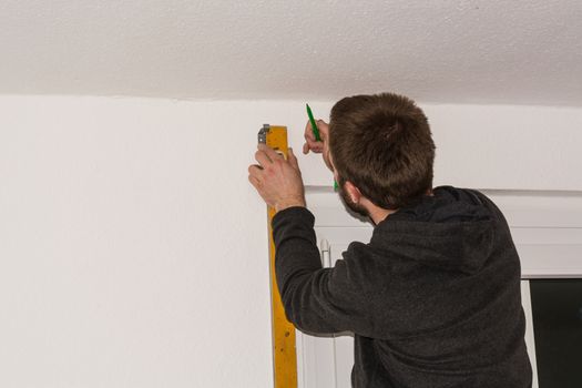 Young craftsman on a ladder with a spirit level and pencil.