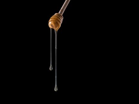 Organic honey flows from dipper. Isolated on black. Copy space. Honey stick with flowing honey