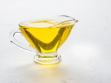 Olive oil in gravy boat on trendy white textured concrete background. Cooking oil in glass jug with copy space