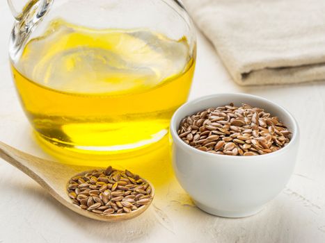 Brown flax seeds in spoon and flaxseed oil in glass bottle on trendy textured white concrete background. Flax oil is rich in omega-3 fatty acid.