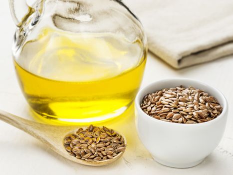 Brown flax seeds in spoon and flaxseed oil in glass bottle on trendy textured white concrete background. Flax oil is rich in omega-3 fatty acid.