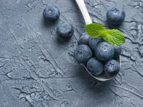 Freshly picked blueberries in spoon closeup. Ripe and juicy fresh blueberry with green mint leaves on textured concrete background. Bilberry on dark background with copyspace. Top view or flat lay