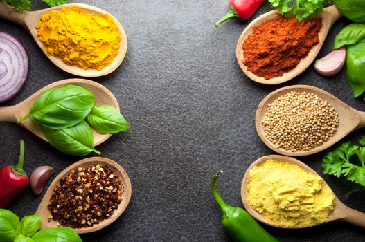 Fresh cooking ingredients including herbs and spices in wooden spoons on a kitchen worktop background