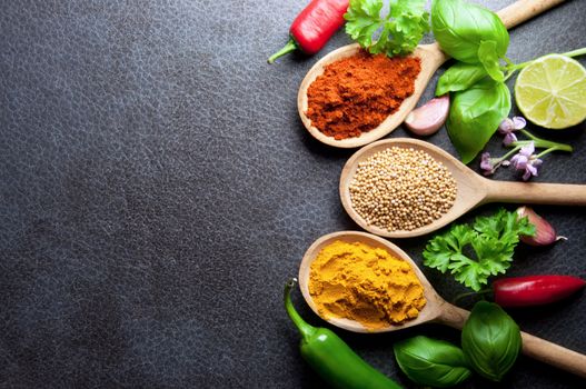 Fresh herbs and spices in wooden spoons kitchen worktop background