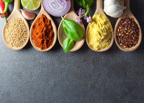 Fresh herbs and spices in wooden spoons kitchen worktop background 