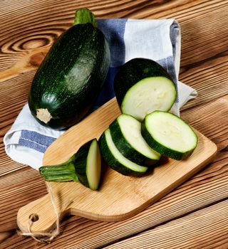 Fresh Raw Zucchini Full Body and Slices on Cutting Board closeup on Wooden background