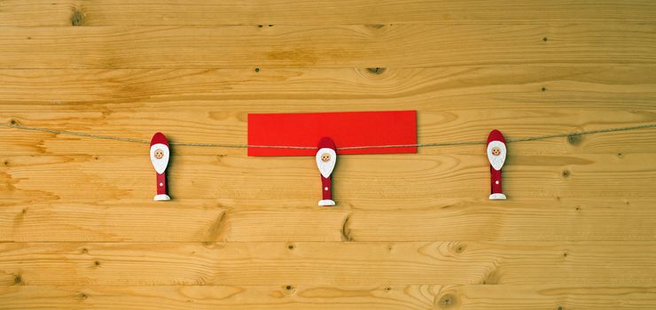 Three christmas men with clothes pegs on a cord on wood