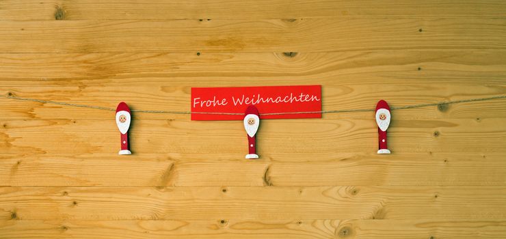 Three christmas men with clothes pegs on a cord on wood and german text for merry christmas