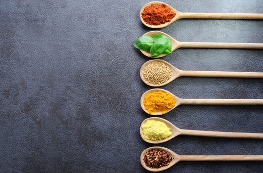 Wooden spoons with various fresh herbs and spices on a kitchen worktop background
