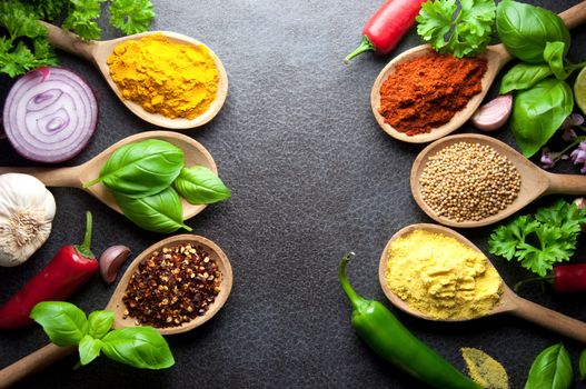 Fresh herbs and spices in wooden spoons kitchen worktop background 