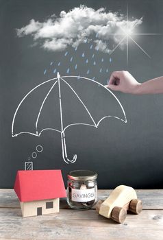 Umbrella being sketched on a chalkboard protecting a house, car and money