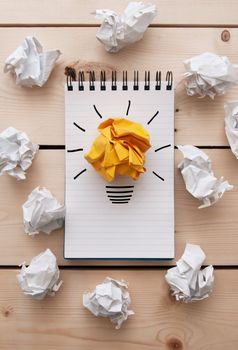 Bright paper light bulb on a notepad between crumpled pieces of paper 