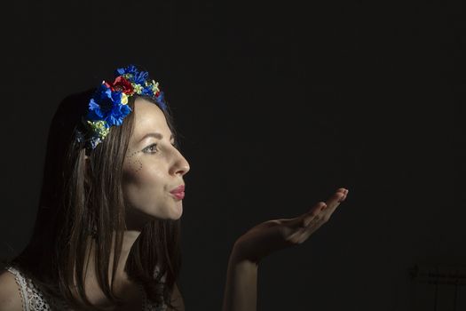 Portrait of a young woman in a wreath of flowers on a black background