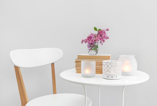 Candle lights, books and flowers on a white table. Elegant home decor.