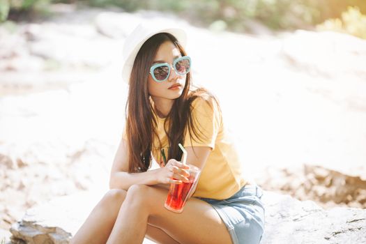 Woman drinking iced drinks outdoors with sand by the sea.