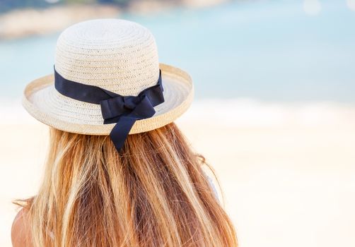 Back view of young woman with a straw hat on beach background