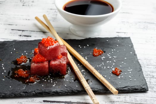 Tuna sashimi dipped in soy sauce with salmon roe, thick salt and dill on slate stone with chopsticks and bowl with soy. Raw fish in traditional Japanese style. Horizontal image.