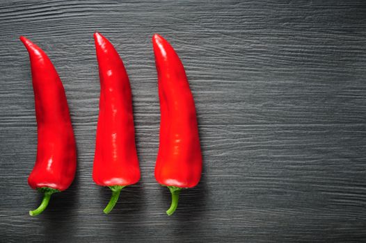 Three ripe sweet red Kapia peppers on dark shale stone background, copy space