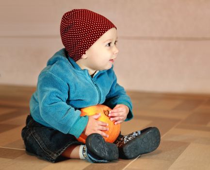 little boy of eight months holding not big orange pumpkin