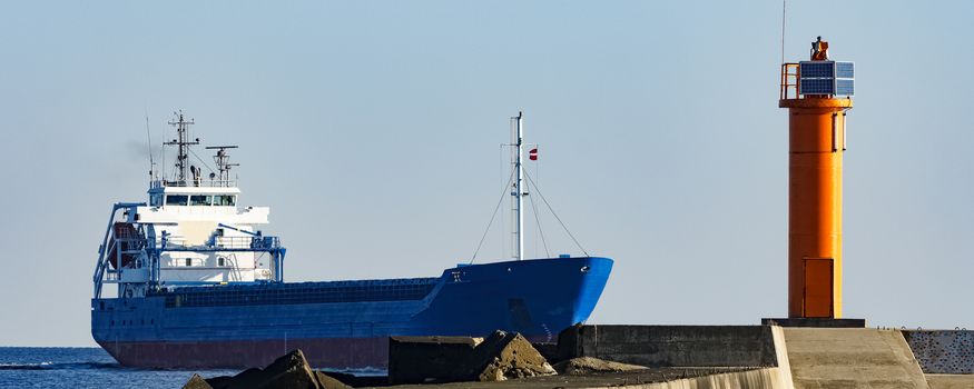 Blue cargo ship sailing against the breakwater dam