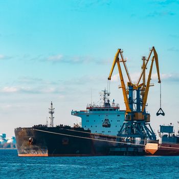 Black cargo ship loading with a coal at the port