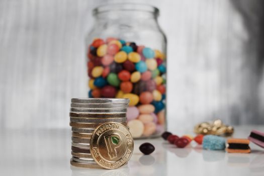 Digital currency physical gold peercoin coin near jelly sweets in glass jar.