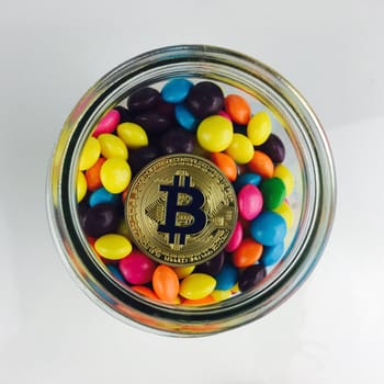 Digital currency physical gold bitcoin coin in glass jar with a sweets.