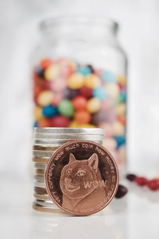 Digital currency physical brass doge coin near money and colorful sweets in glass jar.